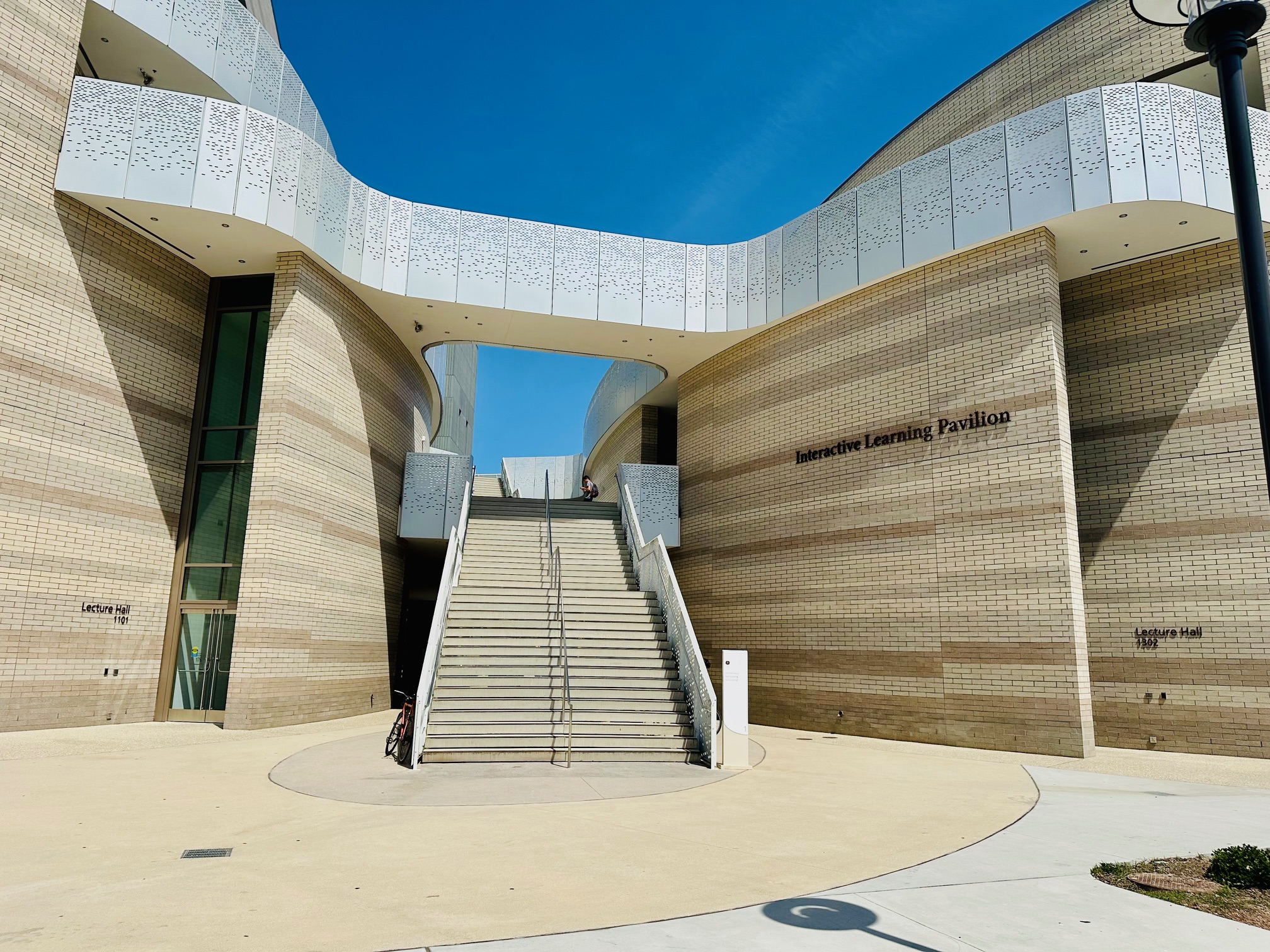 a beige brick building with double stairs bisecting it and a silver perforated railing along the top