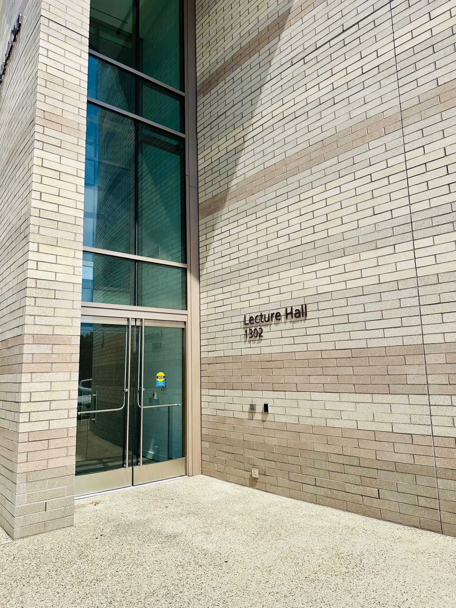 a beige brick building with glass doors and the room number (1302) to the right